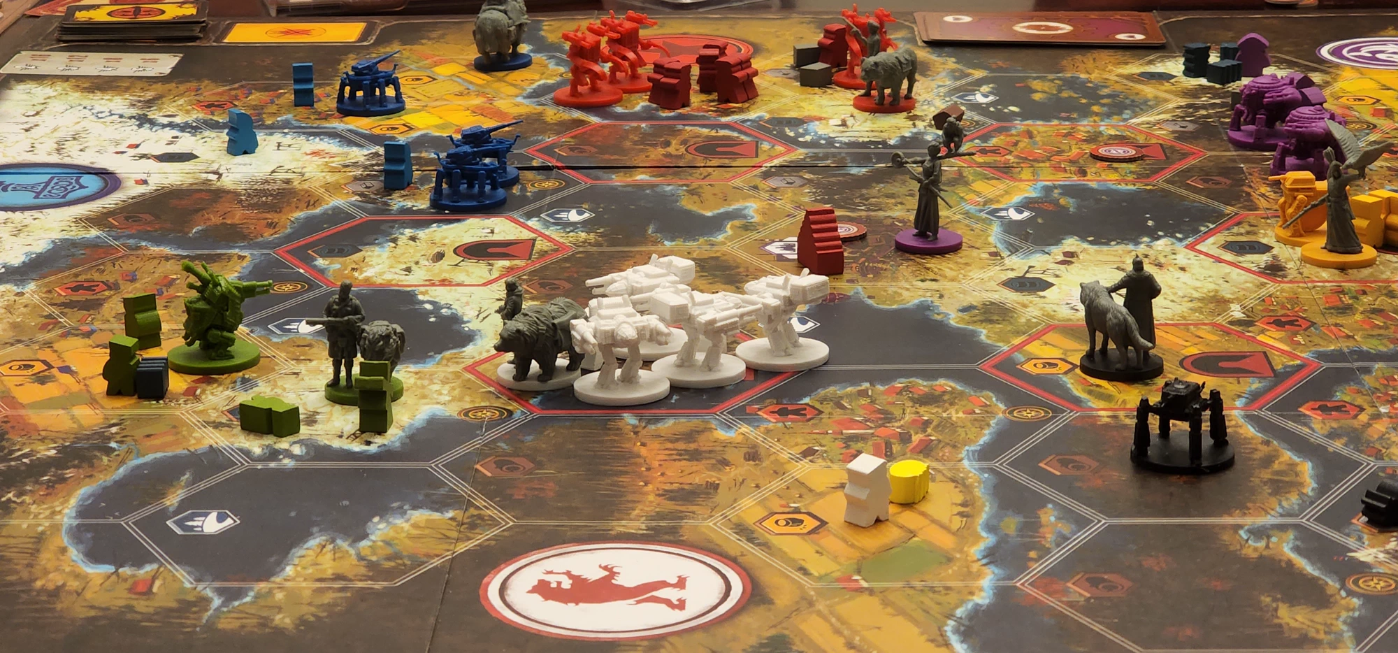A game of Scythe in progress on a table, with its board, player mats, cards, and pieces arranged for play.